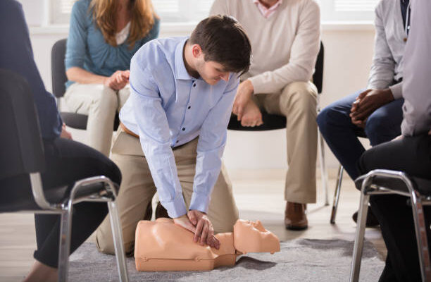 Young Male Instructor Showing CPR Training On Dummy To His Student